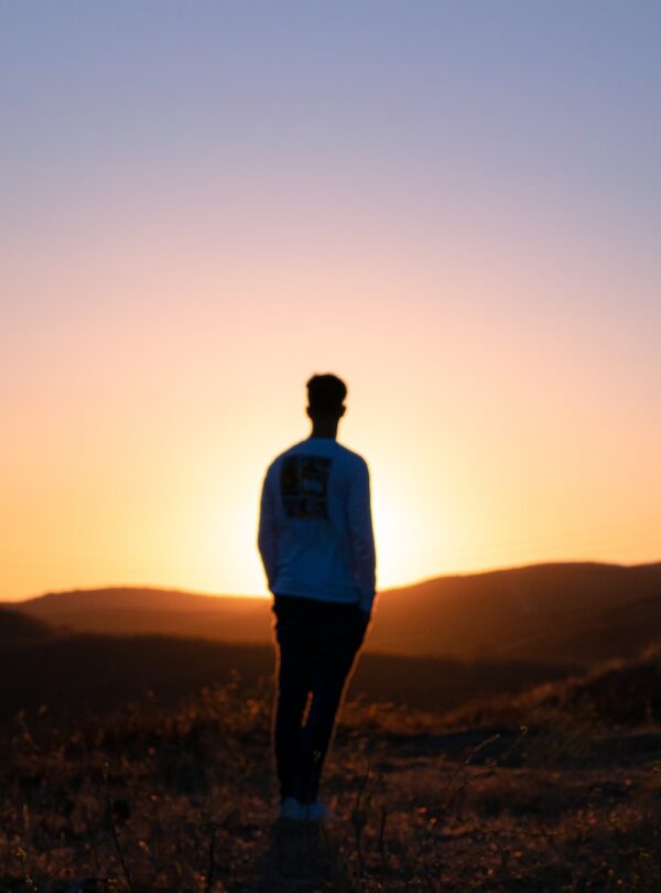 solo man in blue shirt standing on brown field during sunset
