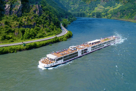 Two-deck river cruise boat with passengers, gliding along a winding, forested river through a valley.